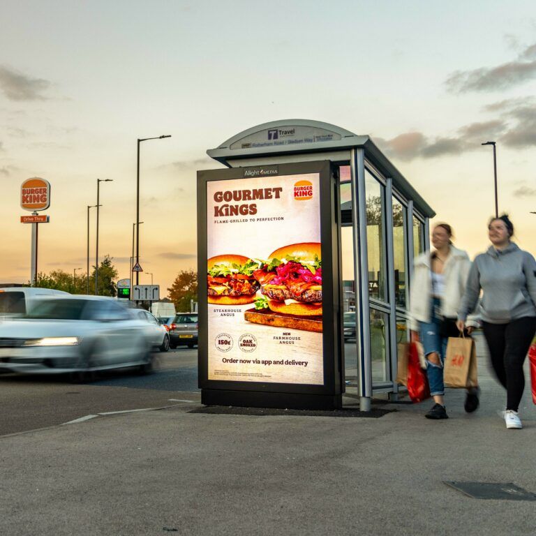 A digital bus shelter screen on a busy road